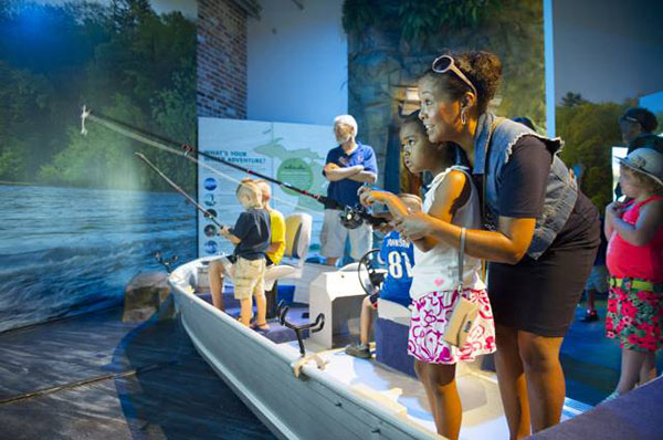Mom helps girl reel in a fish with the fishing simulator at the Outdoor Adventure Center